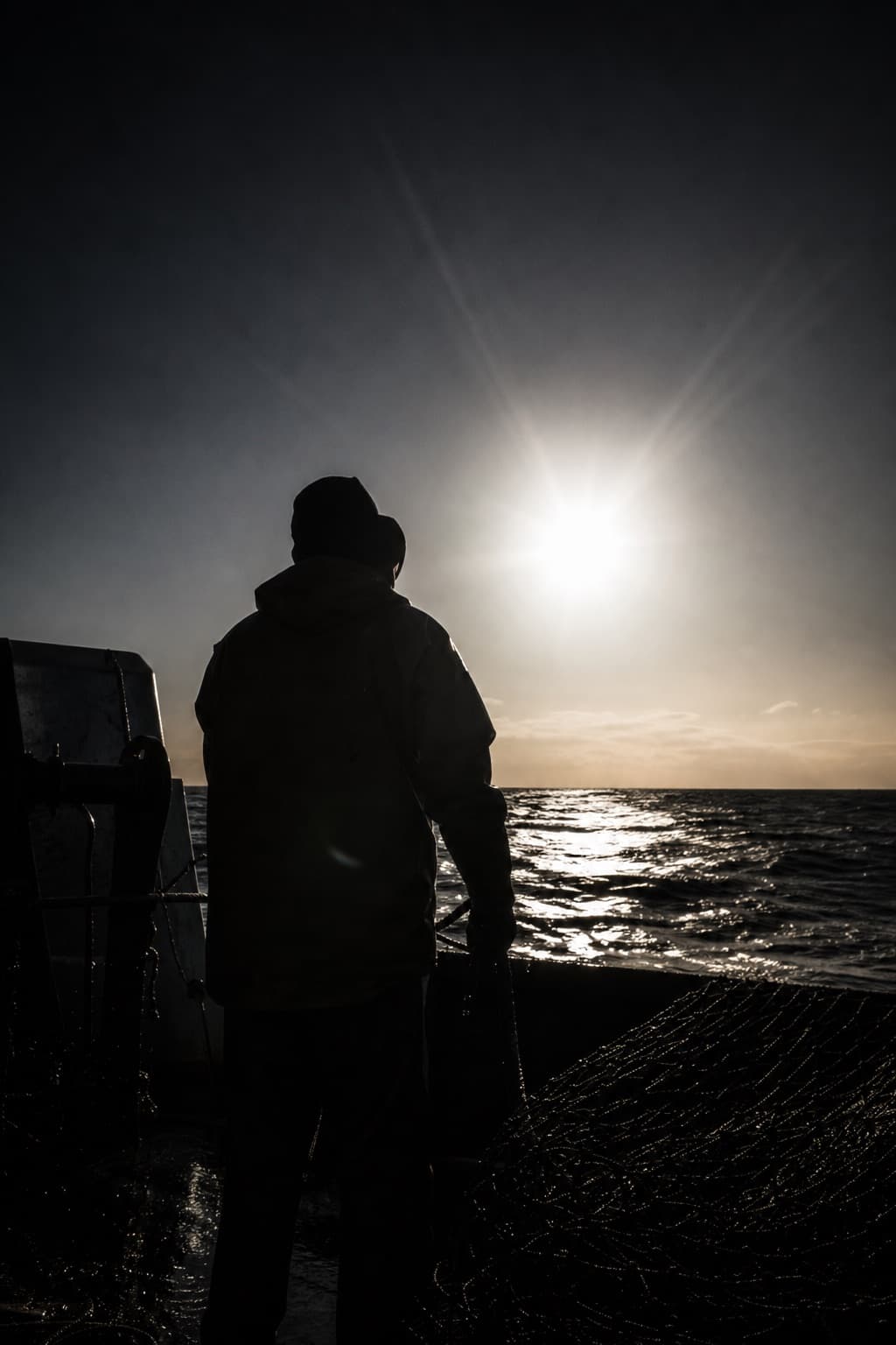 Crew member silhouetted against low sun at sea